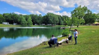 two women and a man fishing at a pond at Muncie RV Resort