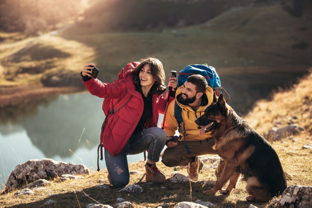Hikers taking a selfie with their dog near a lake.
