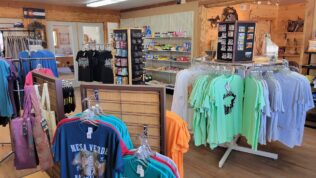 Shirts and bags hanging on racks inside the gift shop at Cortex RV Resort
