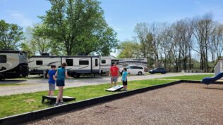 four people playing cornhole next to a playground and RV parking spots at Clarksville RV Resort