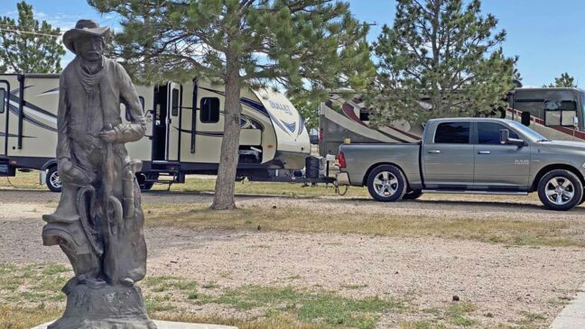 Cowboy statue with RV and Truck at campsite in background.