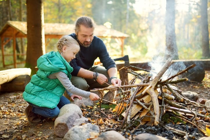 Father showing young daughter how to tend to a fire.