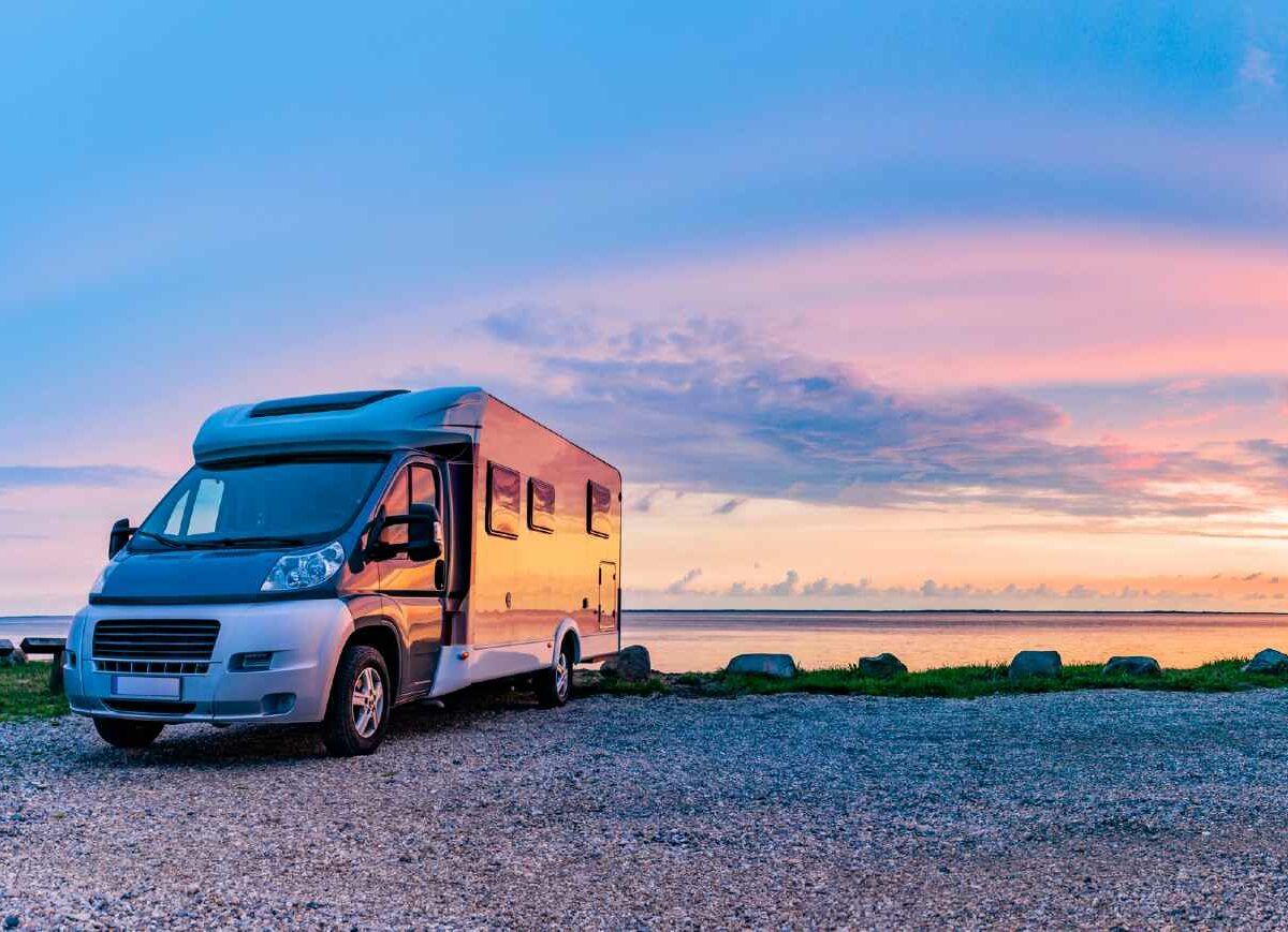 An image of an RV parked along water with a sunset in the background.