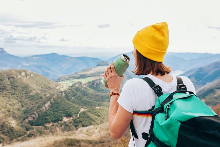 A woman drinking water while looking at a mountain.