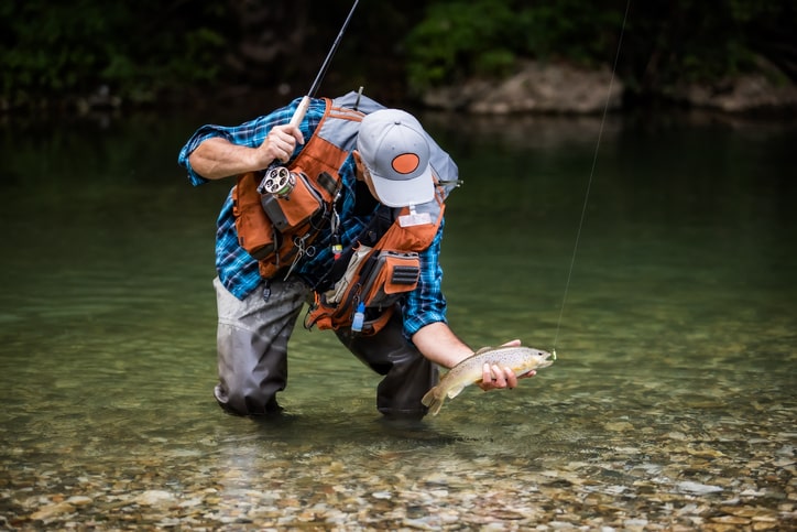 A man standing in a lake while holding fish on a fishing line.