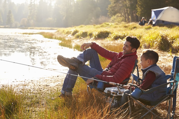 A man teaching his son how to fish near a tent.