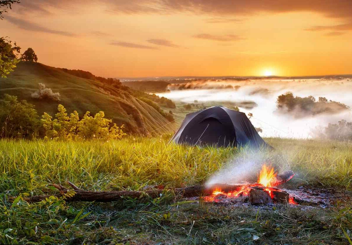 a tent is pitched next to a fire with water and a sunset in the background