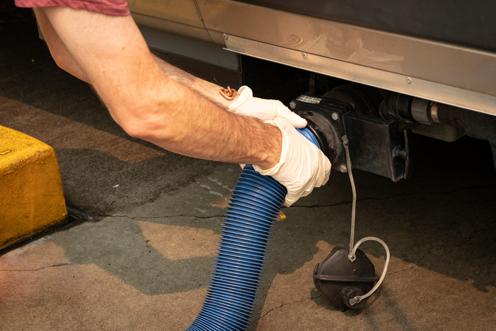 Gloved hands attach a blue hose to drain an RV tank.