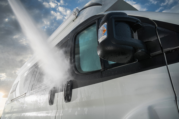 A strong spray of water washes the outside of an RV on a sunny day.