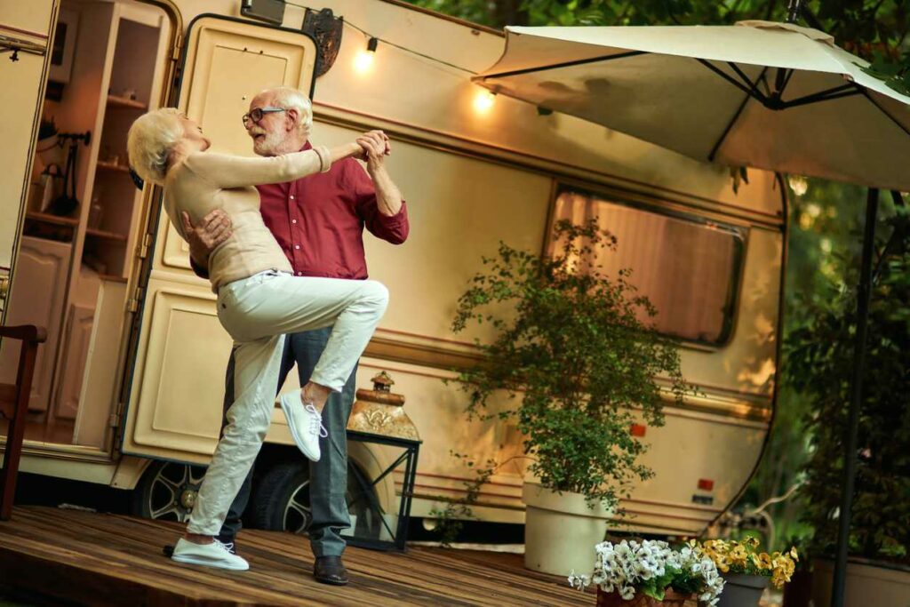 A cheerful, older couple dances outside of their RV in the evening.