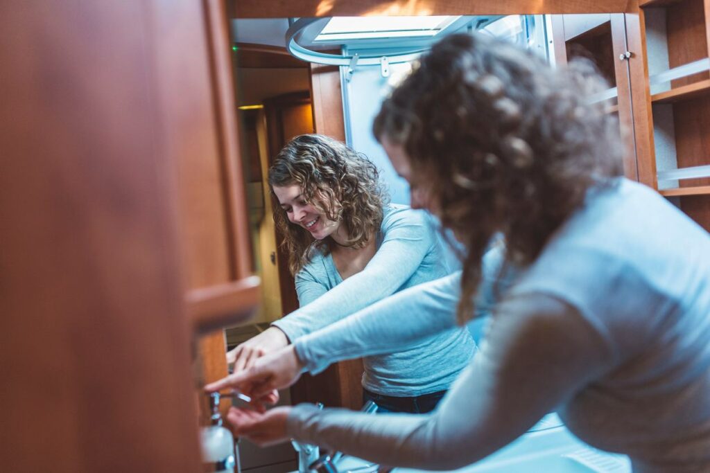A woman is in a luxurious RV bathroom pumping soap into the palm of her hand while standing in front of a large mirror.