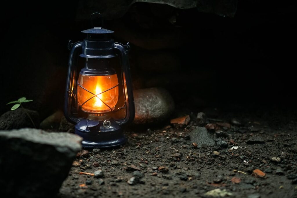 A single lit lantern sits on rocky dirt in the dark