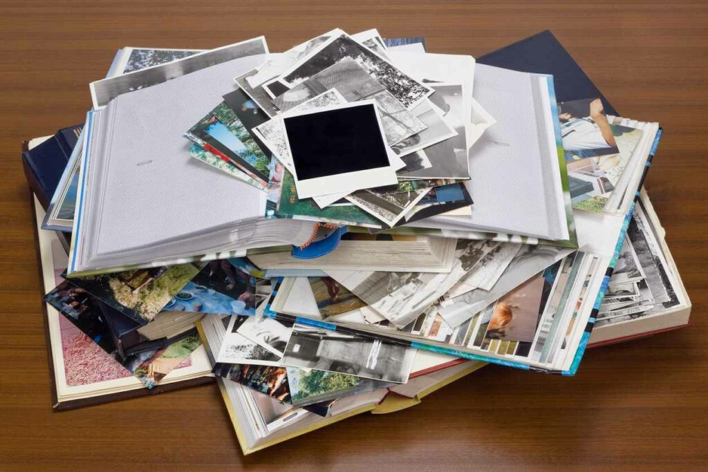 Photo albums sit on a wood floor piled high with photographs to be added to them