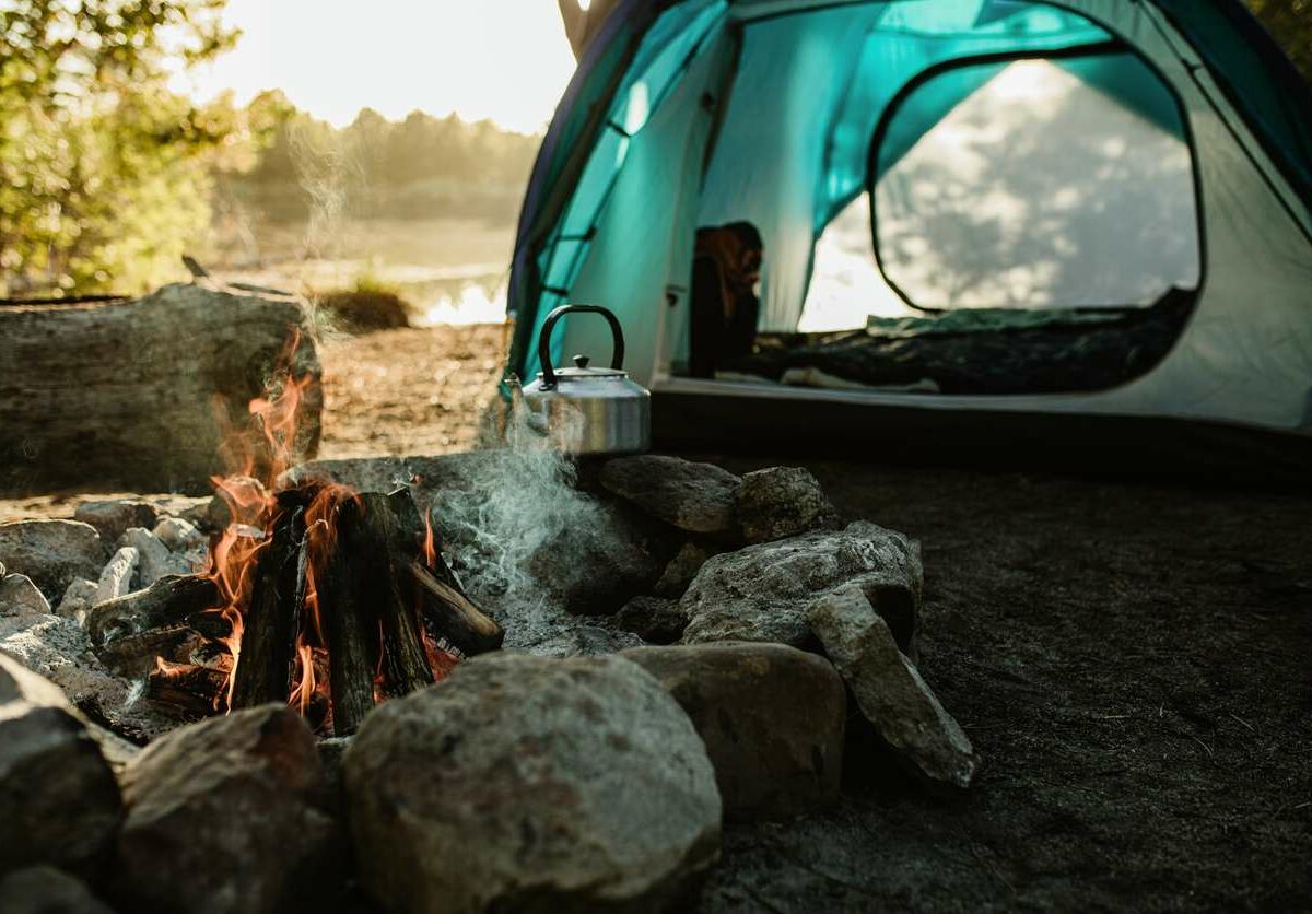 A burning campfire in front of an open tent by the lake.