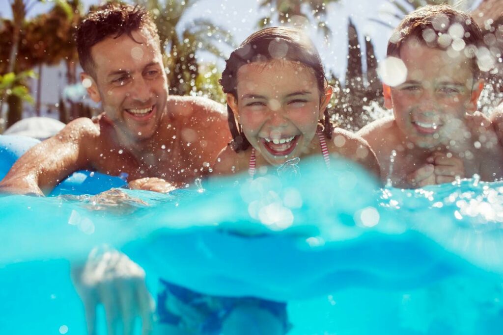 A man and two young children swim in pool