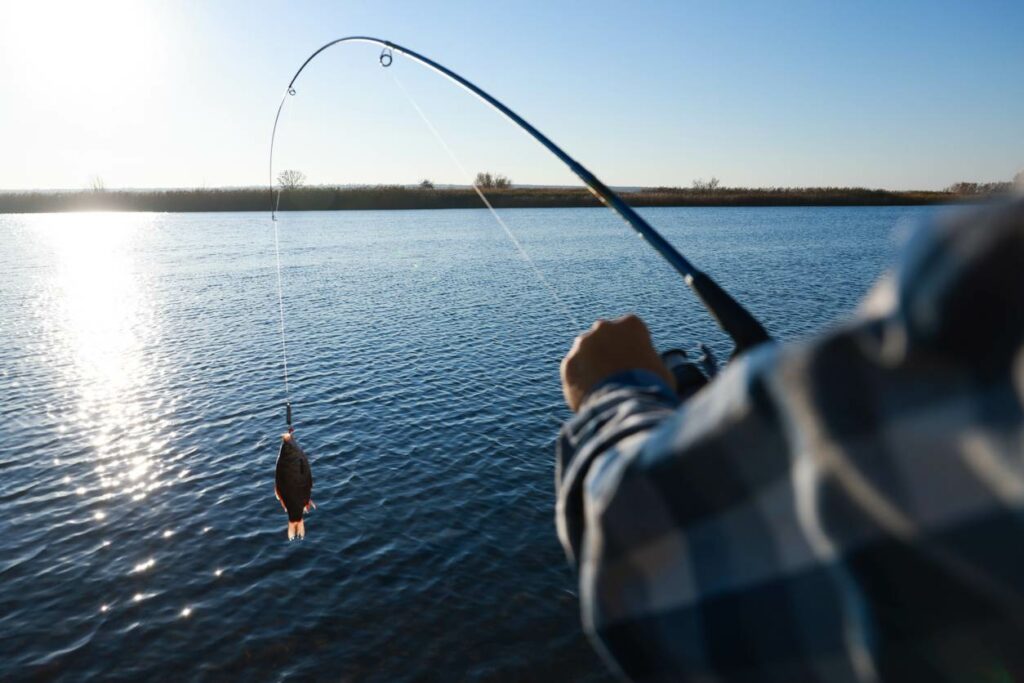 A man fishes in open water with sun in the background