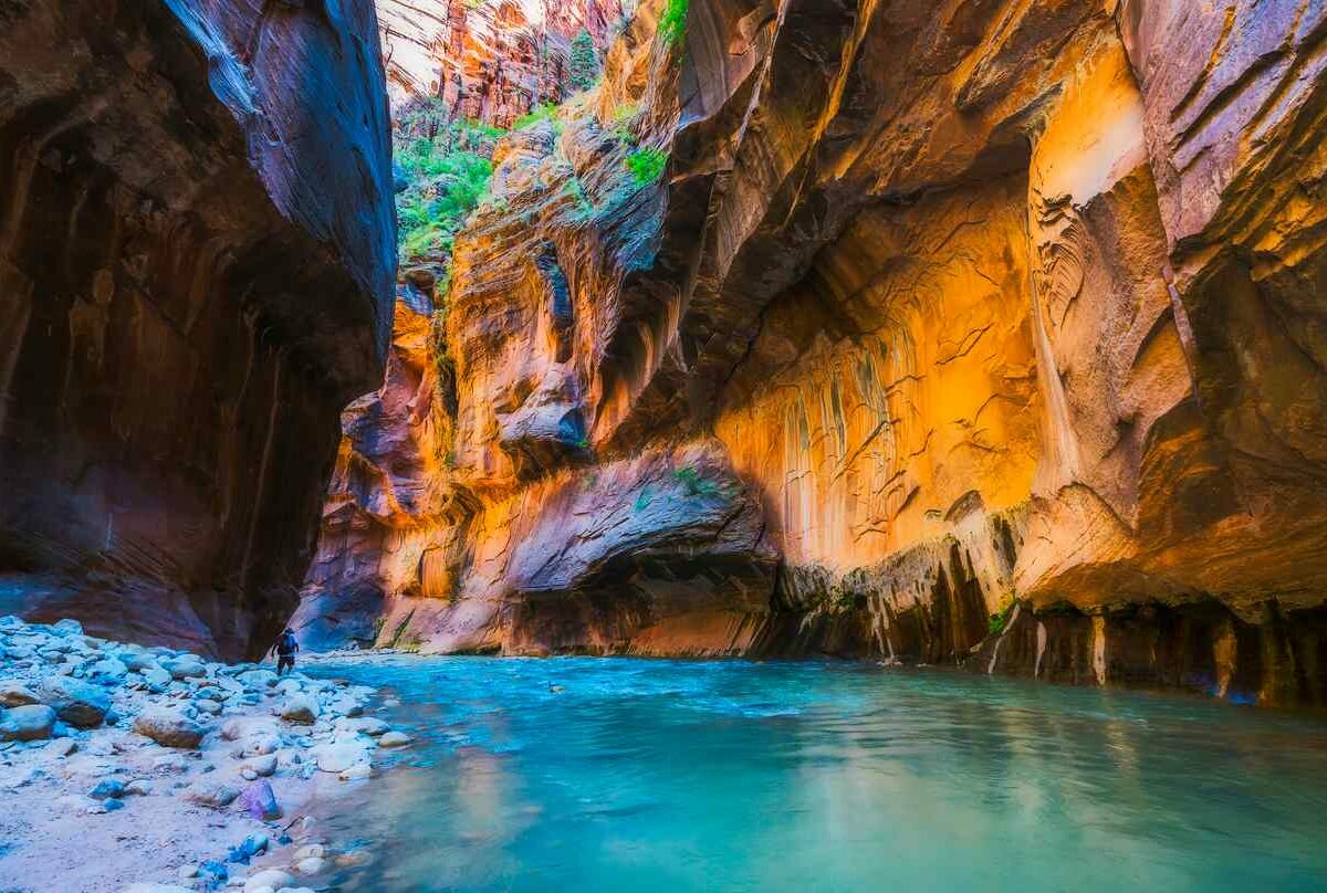 A view at the narrows in Zion National Park shows a stream of blue water surrounded by a large canyon.