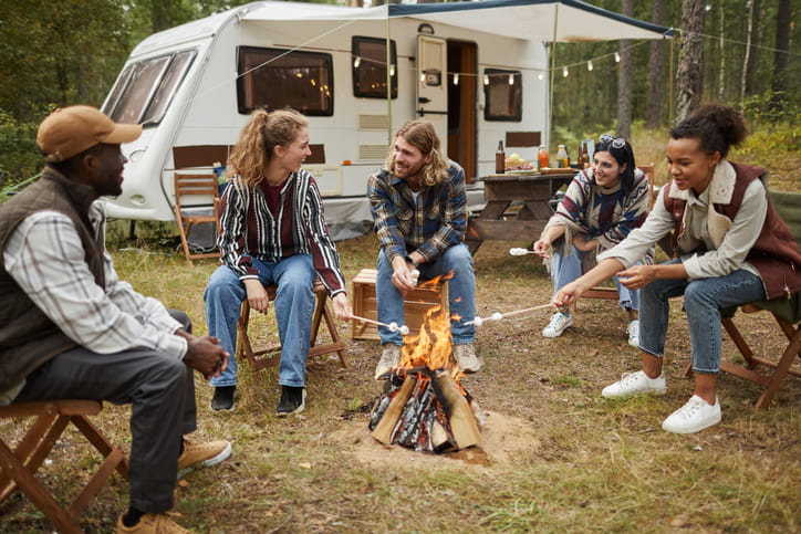 Friends sitting at a bonfire near an RV campsite.