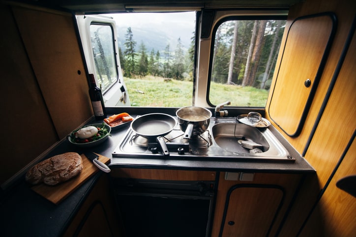 Interior view of the kitchen inside an RV parked at a campsite.