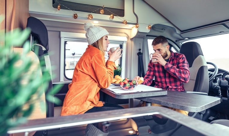 Pair of friends sharing a snack in an RV with winter decorations.