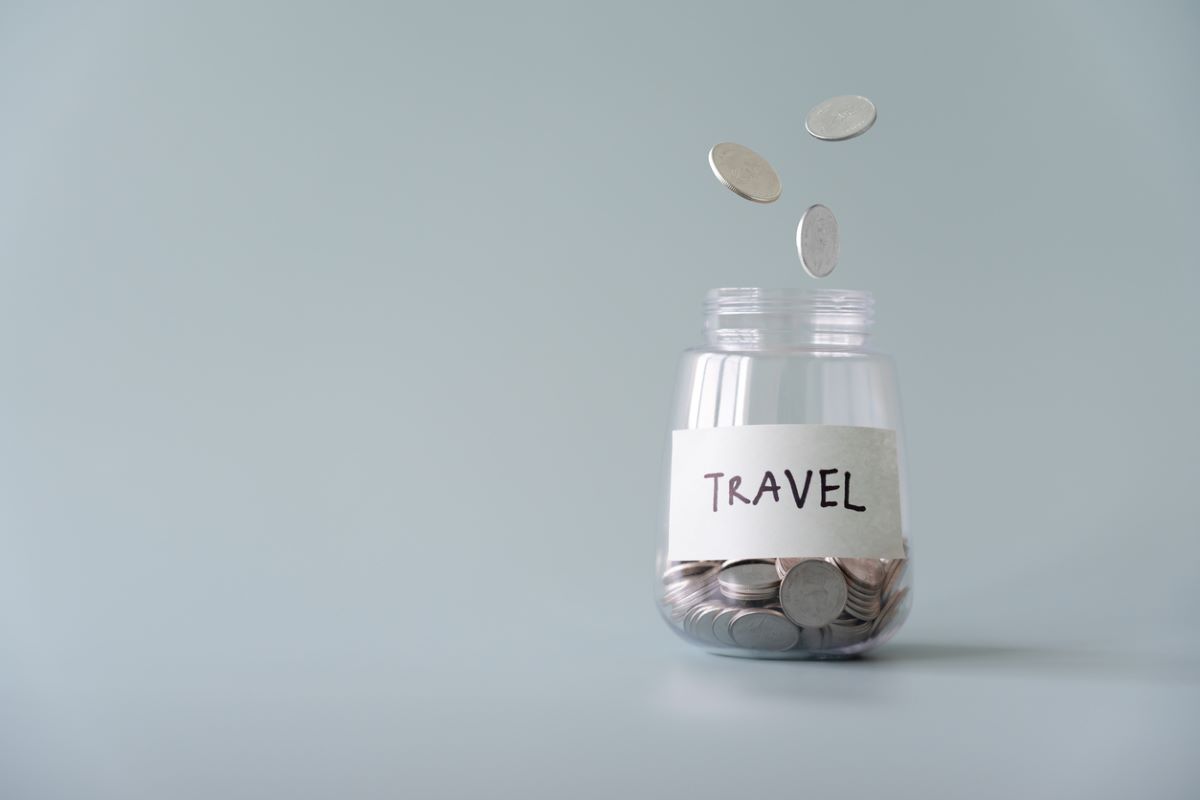 Small glass jar with “travel” label on it with coins inside; savings for a vacation.