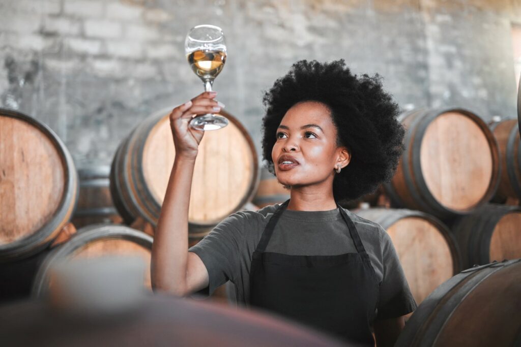 A woman in a wine cellar holding up a wine glass and smiling.