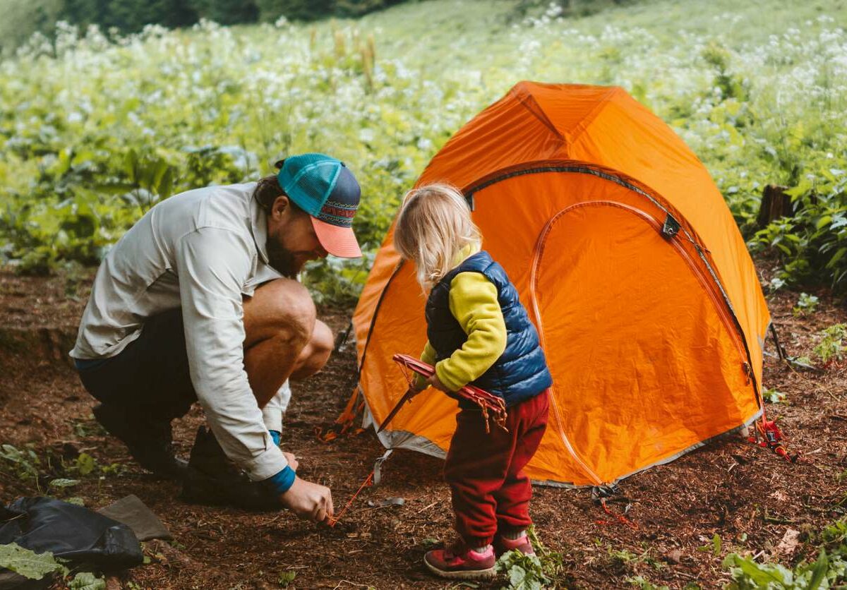 Father and child setting up camping on a durable dirt surface outdoors.