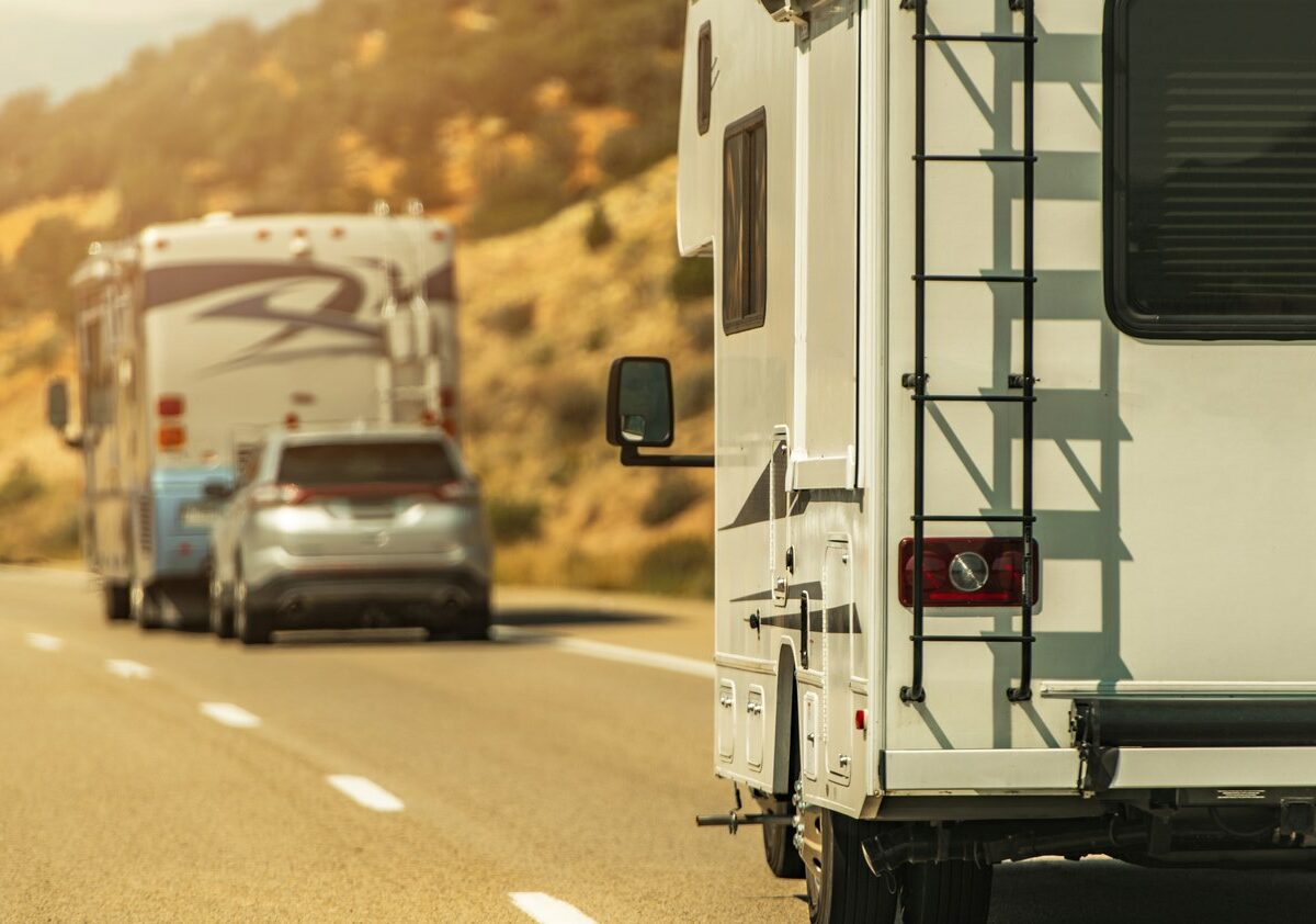 The back view of a pair of RVs driving down the highway.