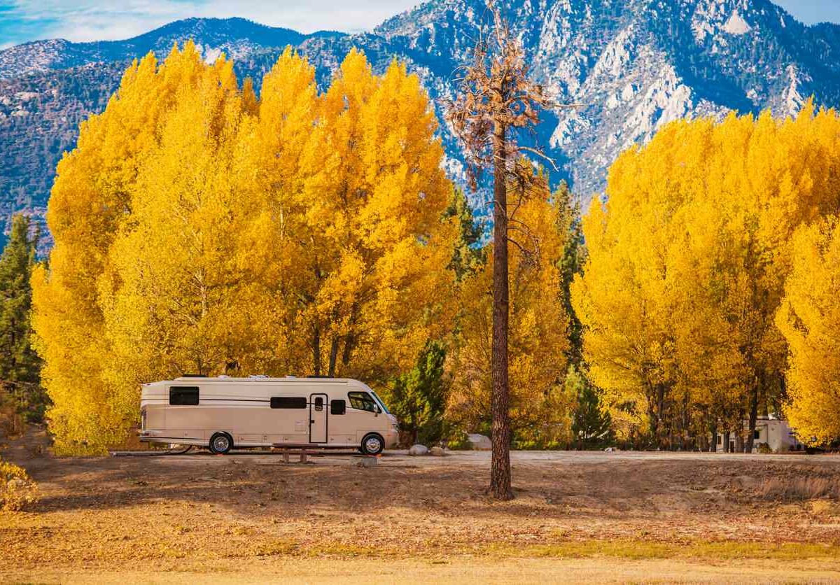 An RV parked outside underneath the autumn trees.