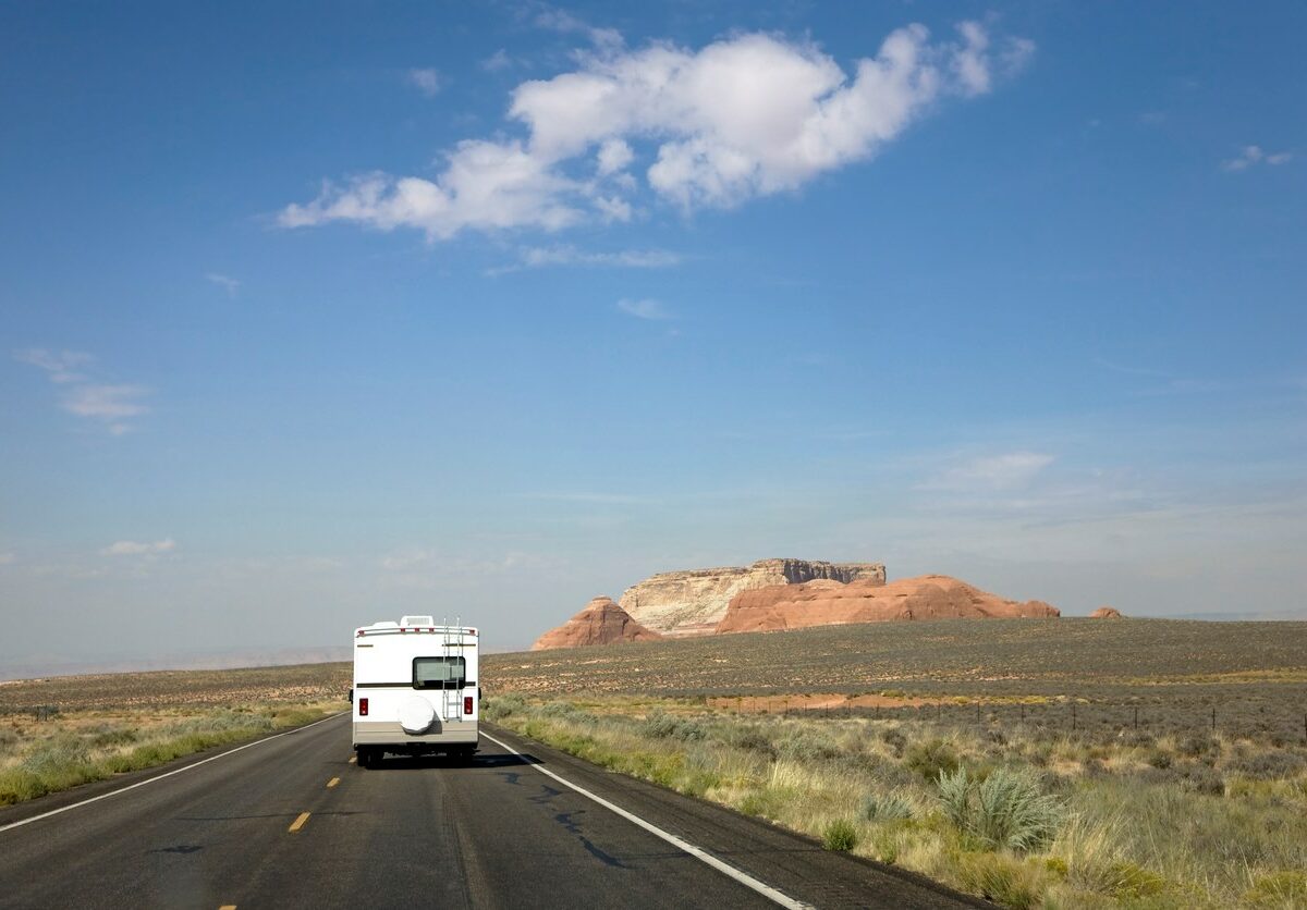 Shot of an RV driving down a highway with a large rock formation in the background.