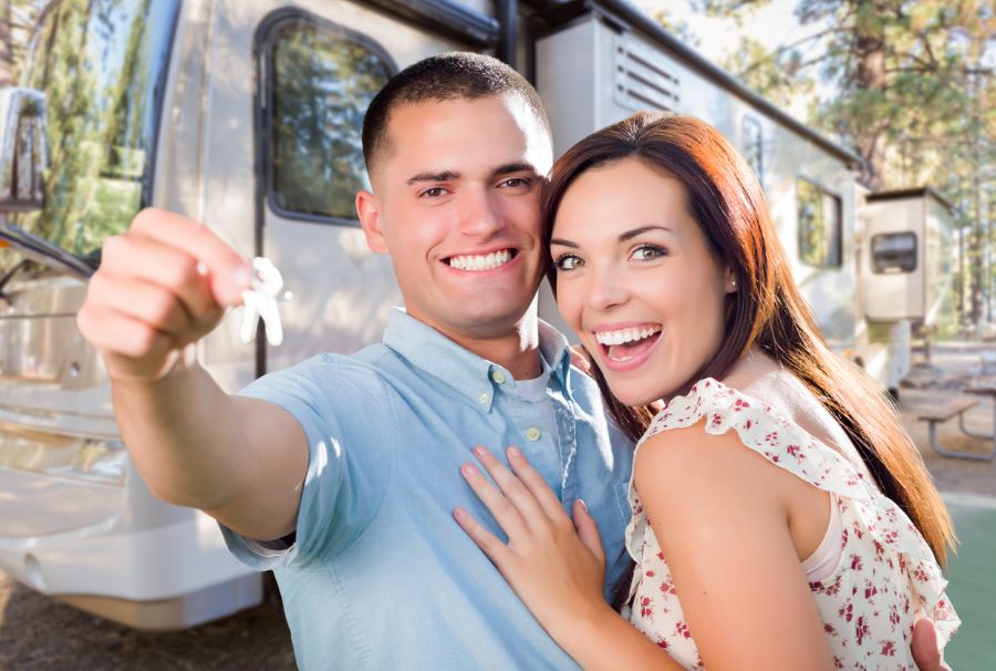 A young, happy couple holding up the keys and ready to adventure in their new RV in the background.