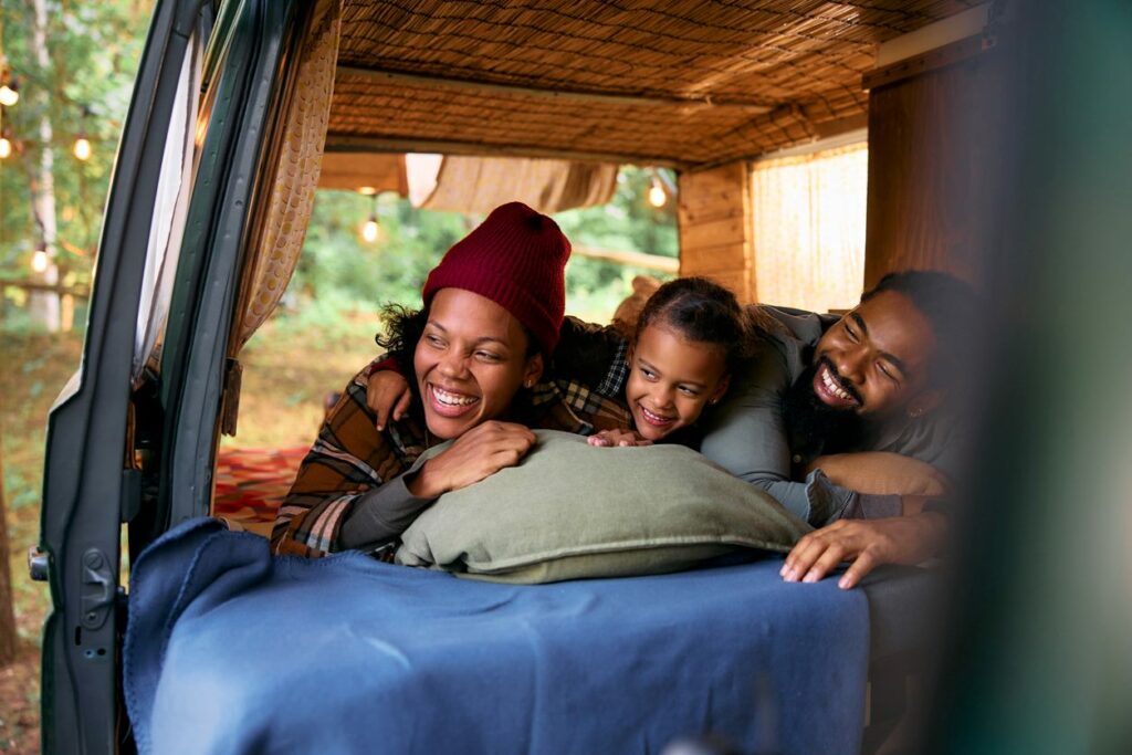 A cheerful family lying on a bed inside an RV at a campground.