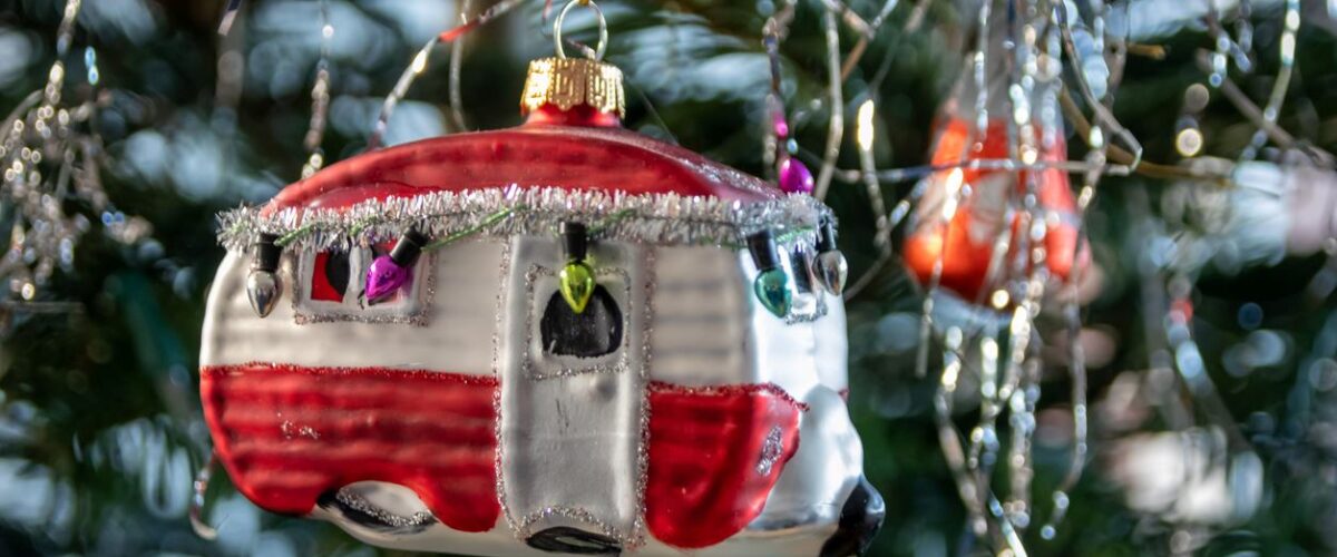 RV camper Christmas ornament hanging from a tree with lights and decorations.