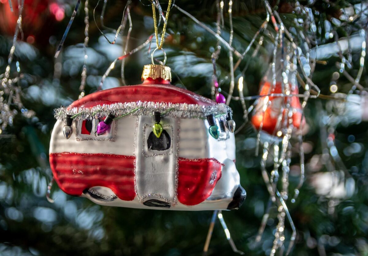 RV camper Christmas ornament hanging from a tree with lights and decorations.