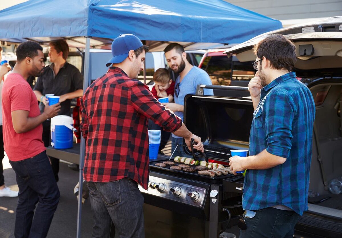 Group of sports fans tailgating and grilling behind their vehicle.