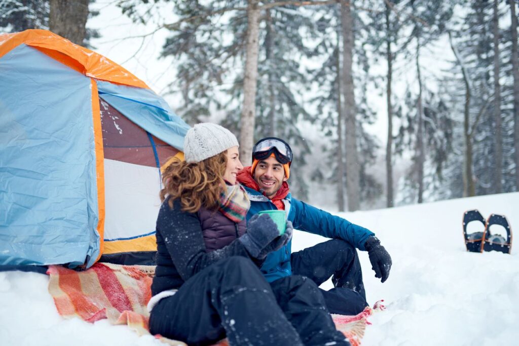 A man and woman enjoying their time in the snowy woods beside their winter tent.