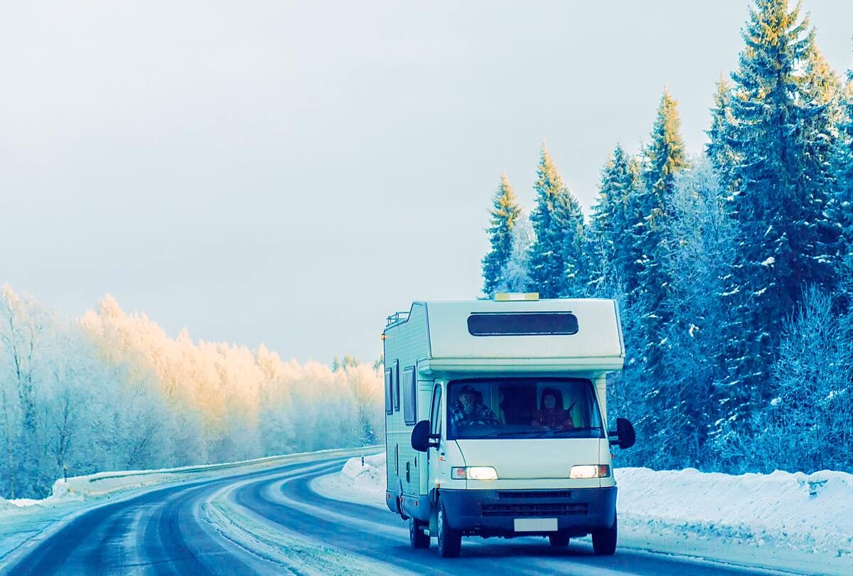 An RV being driven down a snowy road beside a forest.