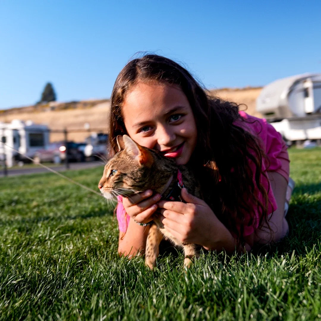 A girl lays down in the grass with her orange cat at Klamath Falls RV Resort by RJourney