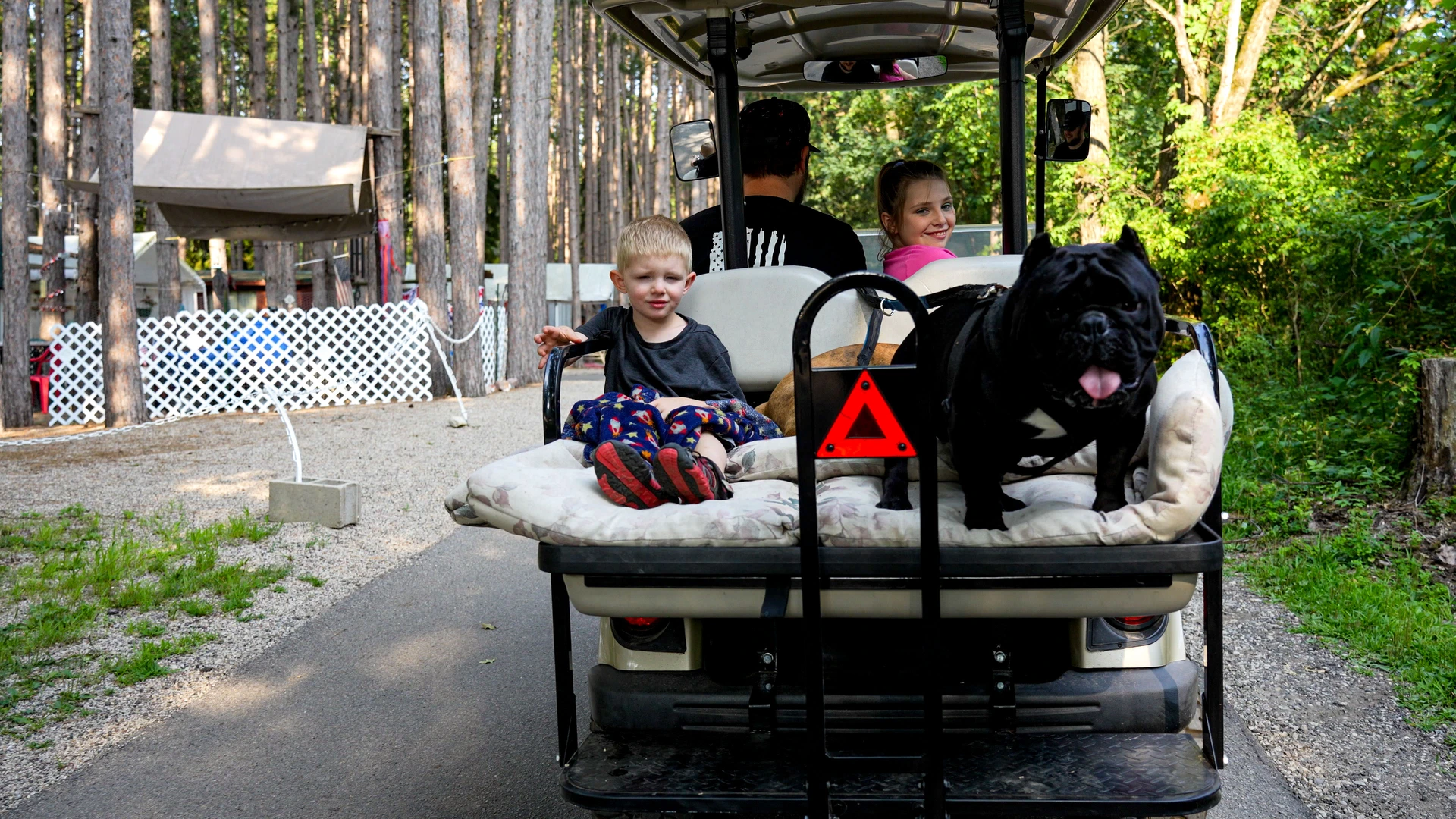 A father, his two kids, and their dog ride leisurely through an RJourney RV park on their golf cart.