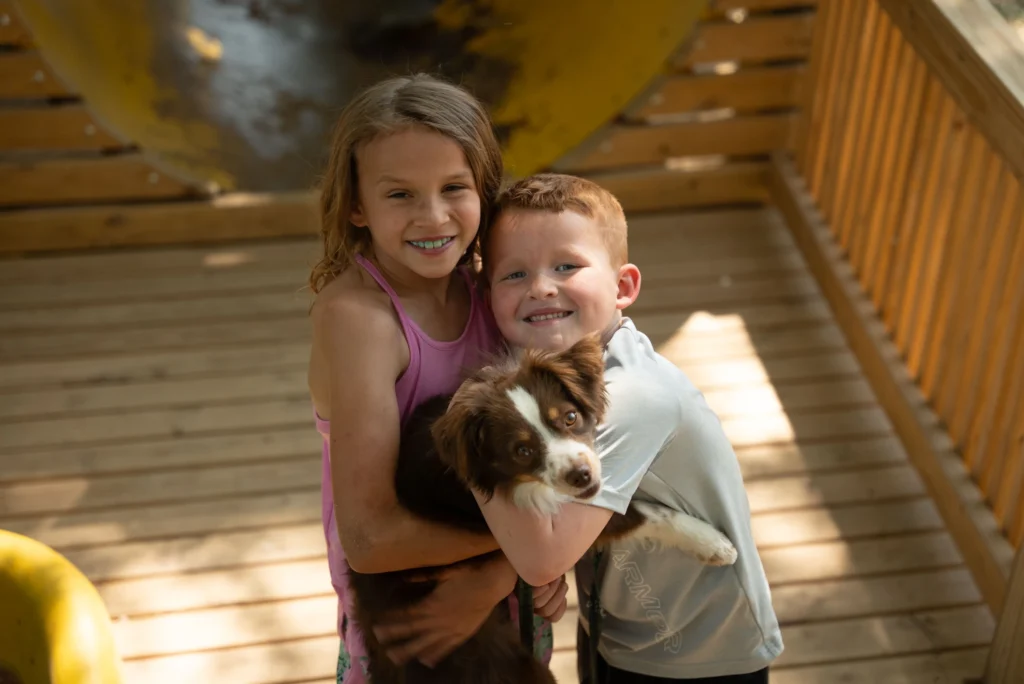 Two children hug their little dog while camping.