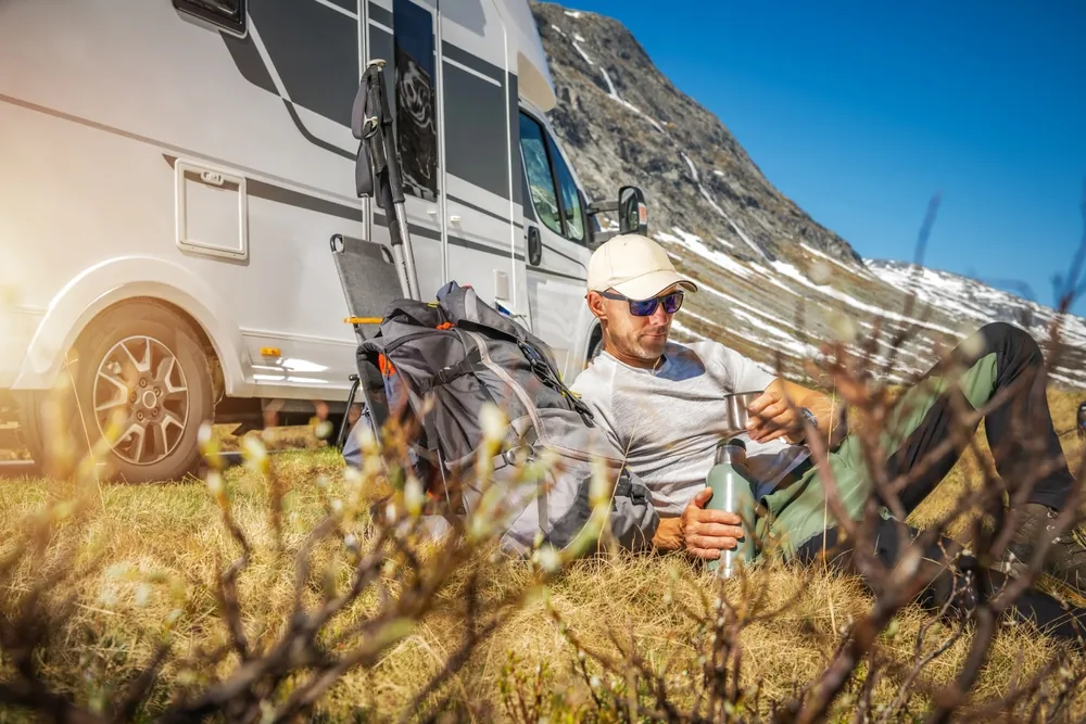 Camper relaxing with a thermos beside his RV at an off-grid mountain campsite