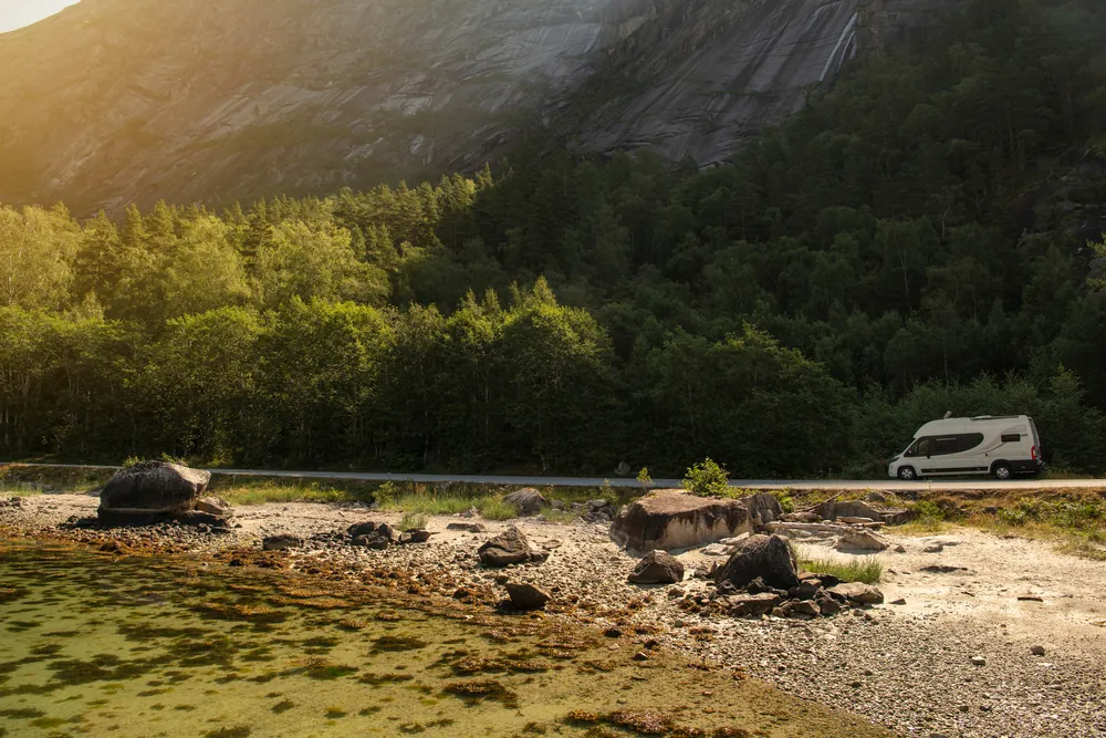 Camper van boondocking beside a river below forested mountains at sunset